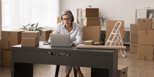 Focused middle aged woman entrepreneur work at storage place, use ecommerce application for small business, check on-line orders, prepare parcels for shipment, chat with customer. Online selling, SME