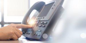 close up employee call center man hand point and press button number telephone voip machine in the office desk for business communication technology and contact us concept