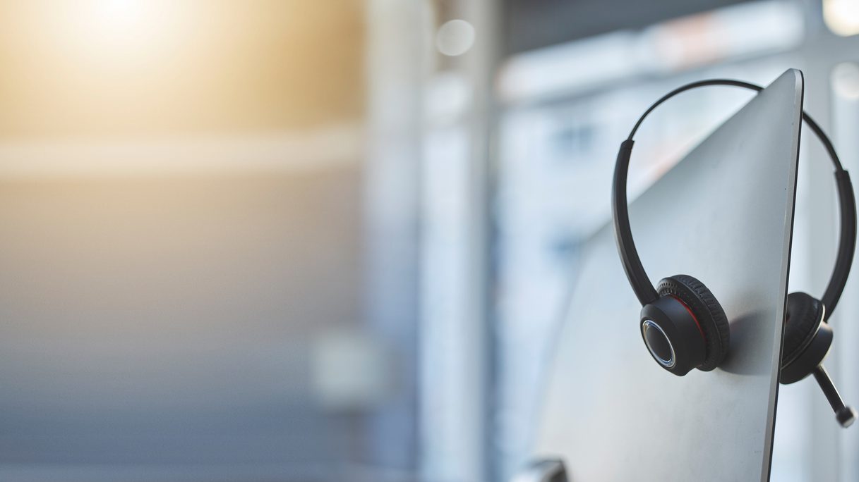 Call center, headset on a computer in an empty office with flare and mockup for communication or assistance. Customer care, support and equipment in a workplace after hours for help or service