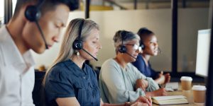 Senior call center consultant, woman and contact us, CRM and talking in customer service, computer at desk. Phone call, telemarketing and diversity, writing in notebook in coworking space and headset