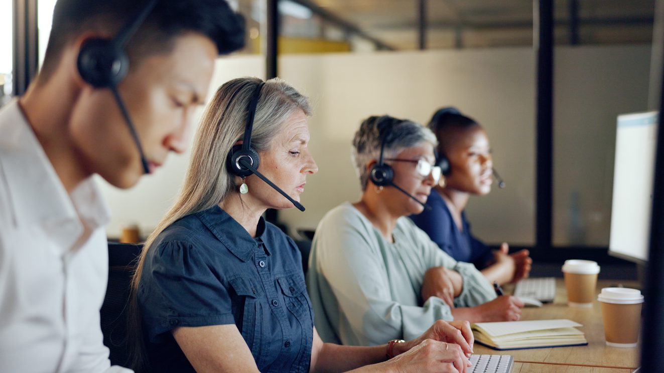 Senior call center consultant, woman and contact us, CRM and talking in customer service, computer at desk. Phone call, telemarketing and diversity, writing in notebook in coworking space and headset