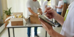 Manager of charity organization taking notes on tablet computer when volunteers packing boxes for refugees