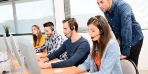 Group of young people with desktop computer in row and headset training with teacher instructor in customer service call support helpline