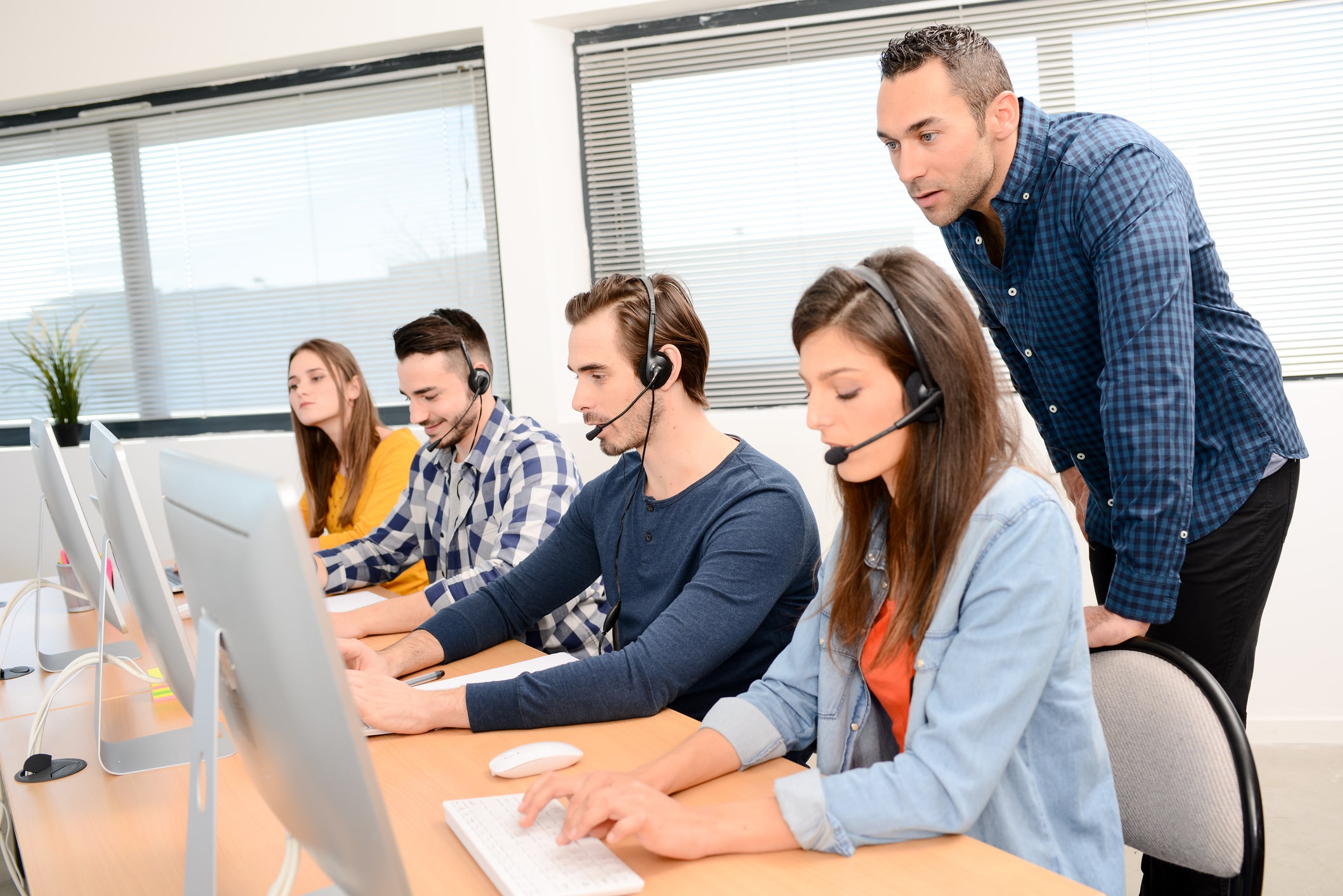 Group of young people with desktop computer in row and headset training with teacher instructor in customer service call support helpline