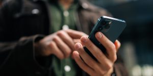 Close-up hands of unrecognizable man holding and using smartphone standing on city street, browsing internet, checking social media, using mobile application