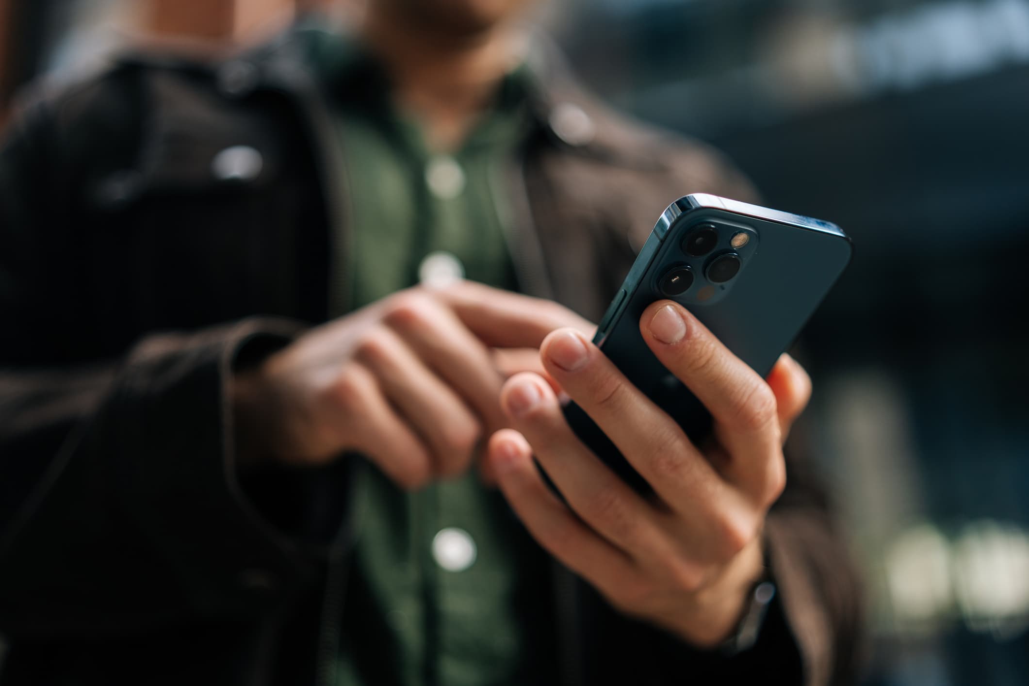 Close-up hands of unrecognizable man holding and using smartphone standing on city street, browsing internet, checking social media, using mobile application